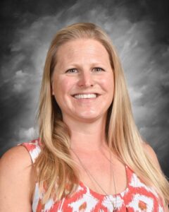Portrait of a smiling woman with long blonde hair, wearing a colorful patterned shirt, against a gray background. Ideal for representing a friendly and approachable professional.