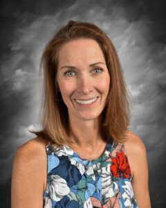 Professional headshot of a smiling woman with shoulder-length brown hair, wearing a colorful floral blouse. The background is softly blurred, enhancing her friendly expression. Ideal for business profiles or personal branding.