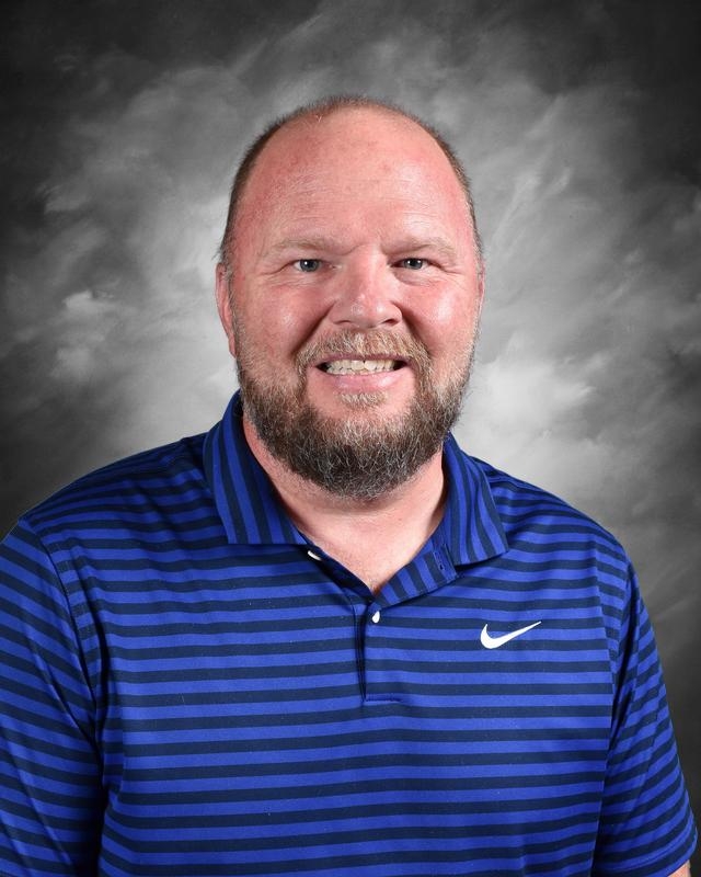 Smiling man with a beard wearing a blue striped polo shirt, posing against a gray background. Ideal for profiles or team introductions.