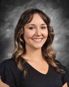 Smiling woman with wavy brown hair wearing a black shirt, posing against a gray background. Ideal for professional profiles or personal branding.