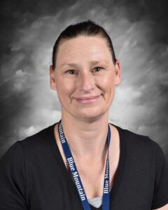 Portrait of a smiling woman wearing a black shirt and a Blue Mountain lanyard, set against a soft gray background.
