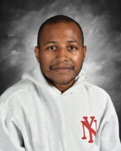 Portrait of a man wearing a light gray hoodie with a red logo, smiling against a soft gray background. The image focuses on his friendly expression and features, making it suitable for professional profiles or team introductions.