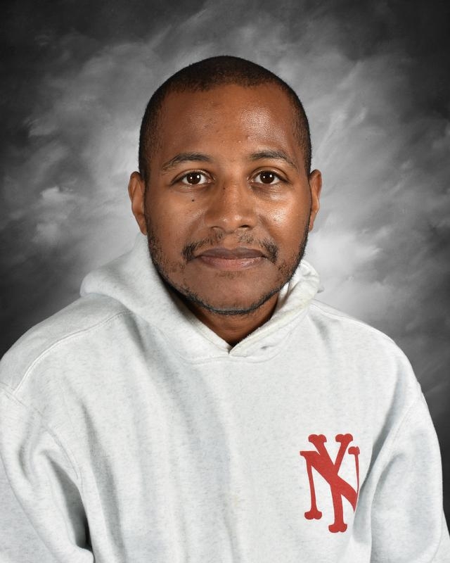 Portrait of a man wearing a light gray hoodie with a red logo, smiling against a soft gray background. The image focuses on his friendly expression and features, making it suitable for professional profiles or team introductions.